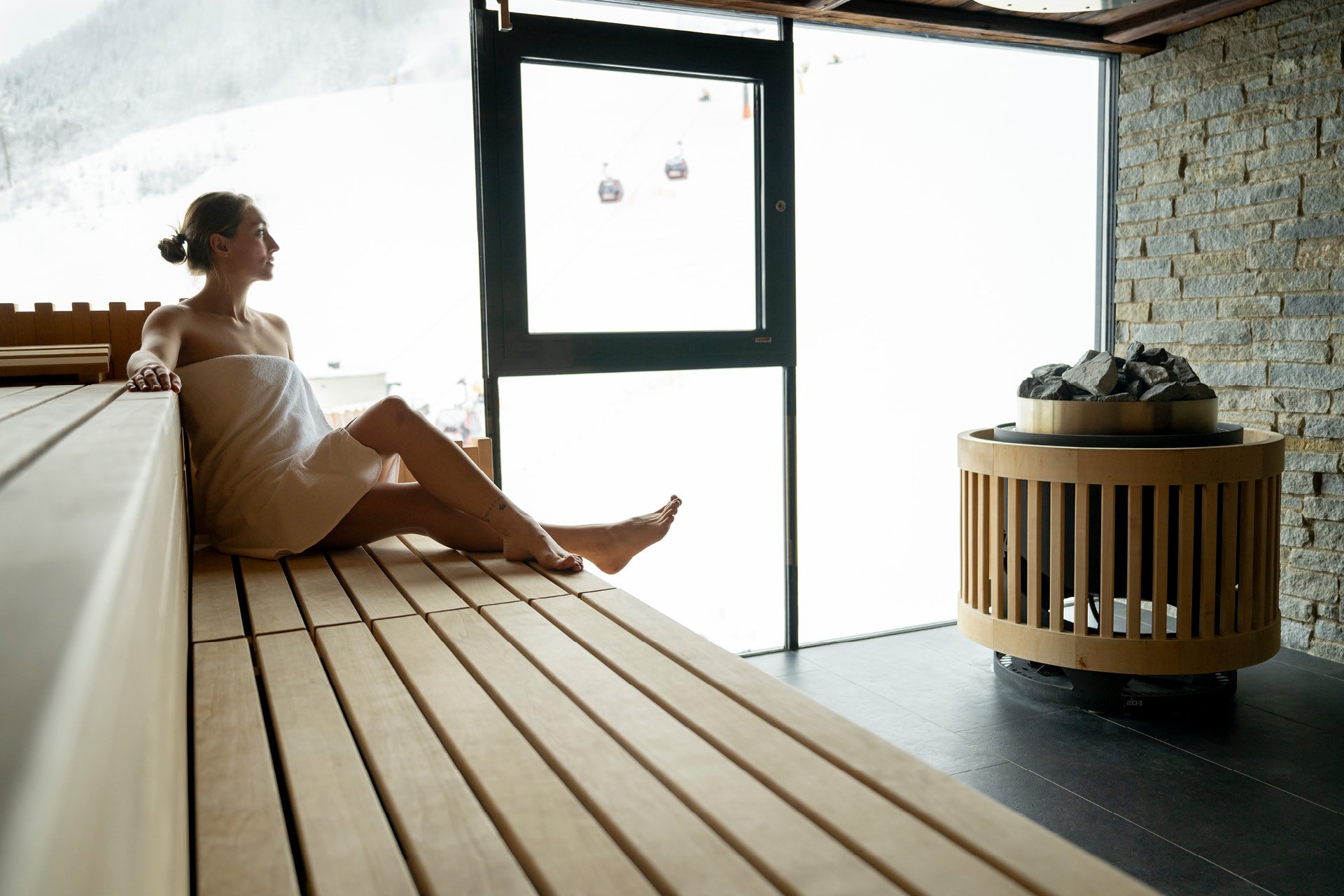 Frau in Sauna mit Piste im Hintergrund