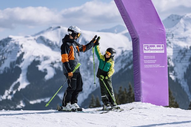 Erwachsener macht High Five mit Kind auf der Piste in Saalbach Hinterglemm