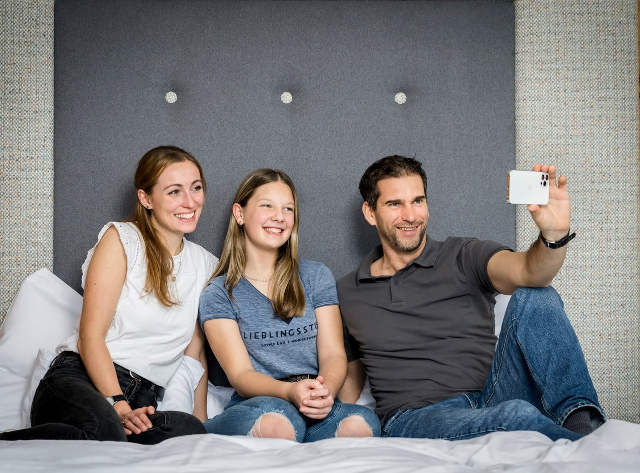 familie-zimmer Familie sitzt am Bett und macht ein Selfie mit dem Smartphone