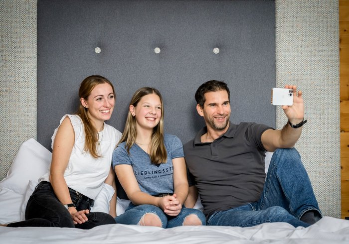 Familie sitzt am Bett und macht ein Selfie mit dem Smartphone