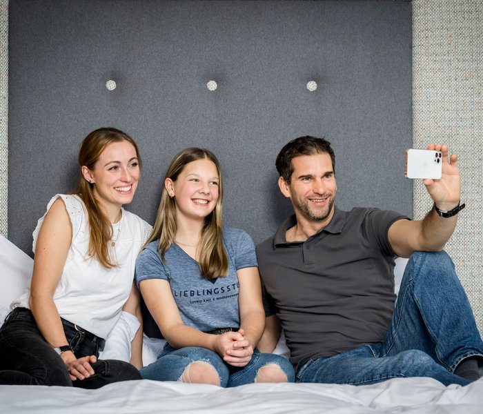 Familie sitzt am Bett und macht ein Selfie mit dem Smartphone