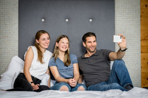 Familie sitzt am Bett und macht ein Selfie mit dem Smartphone