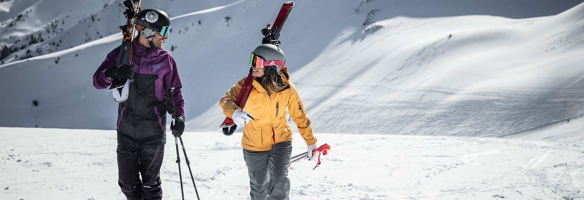 Paar mit Ski auf den Schultern vor Bergpanorama