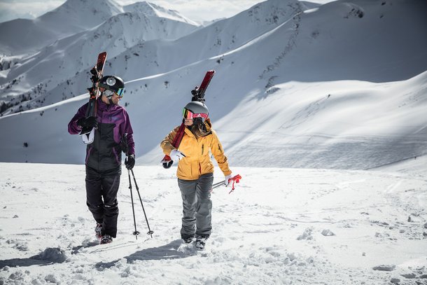 Paar mit Ski auf den Schultern vor Bergpanorama