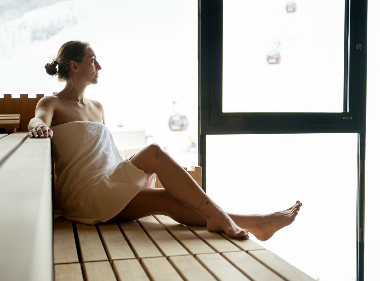 panorama-sauna-header Frau in Sauna genießt Ausblick auf die Piste von der Panorama Sauna aus
