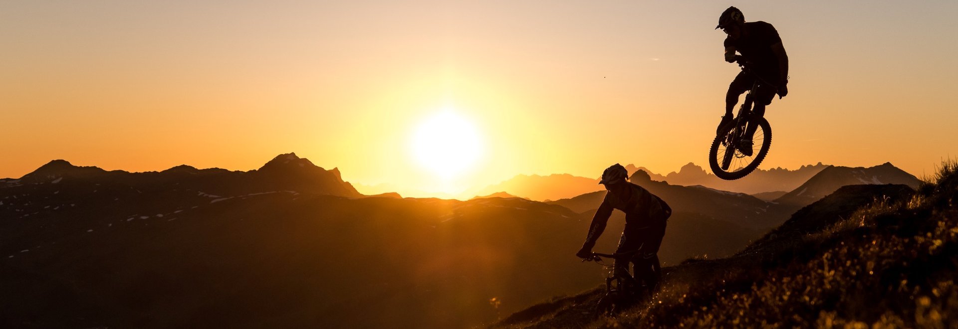 Radfahrer bei Sonnenuntergang in der Bergwelt von Saalbach Hinterglemm bei orangenem Licht