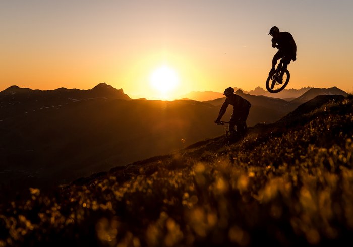 Radfahrer bei Sonnenuntergang in der Bergwelt von Saalbach Hinterglemm bei orangenem Licht